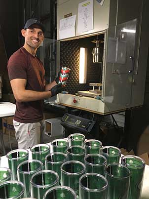 Ron Walters, COO of Freeheart Drinkware, removes a fresh tumbler from an Ultrasonic welder which seals each tumbler with the decoration inside.